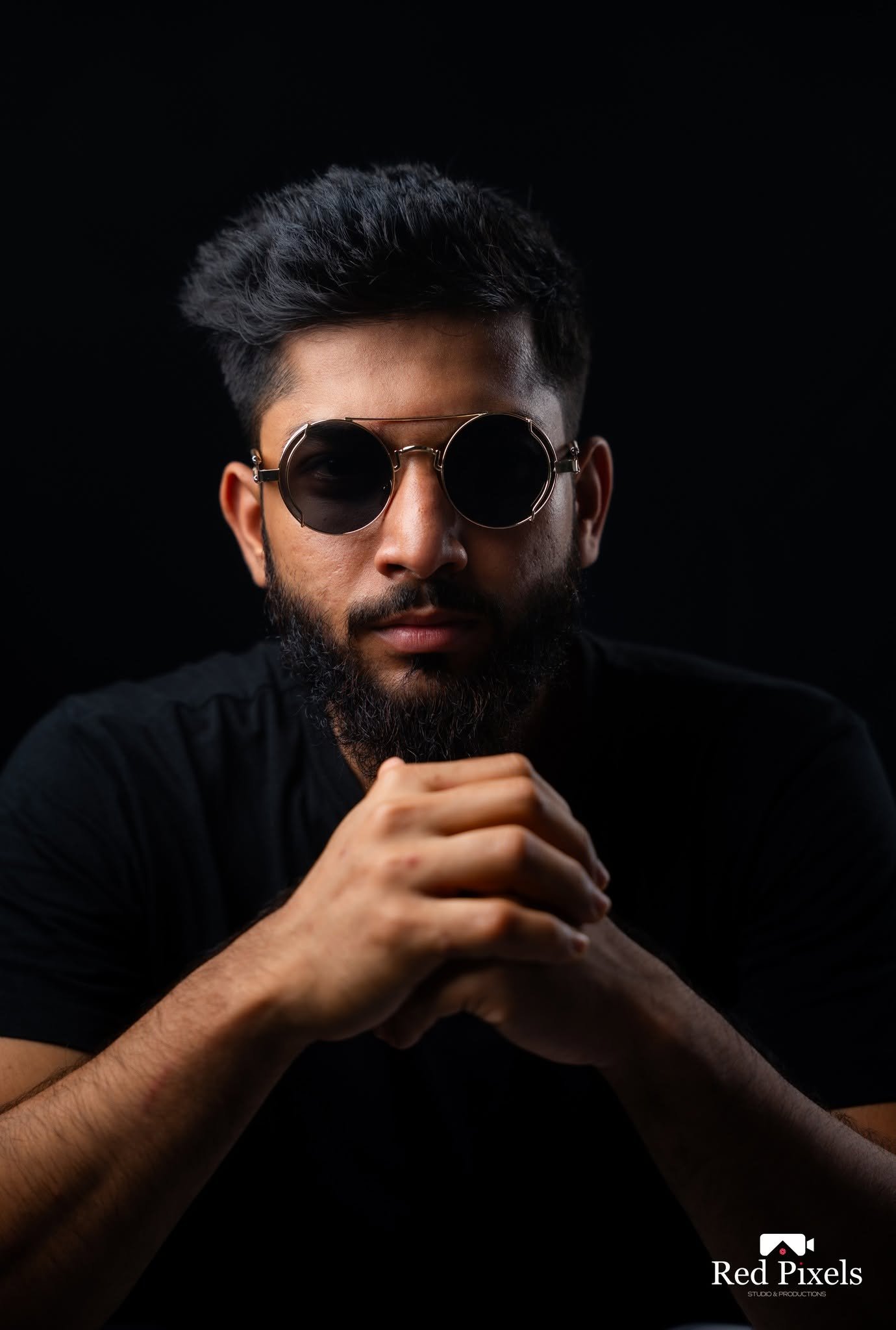 Studio portrait of a man in round sunglasses against a black backdrop