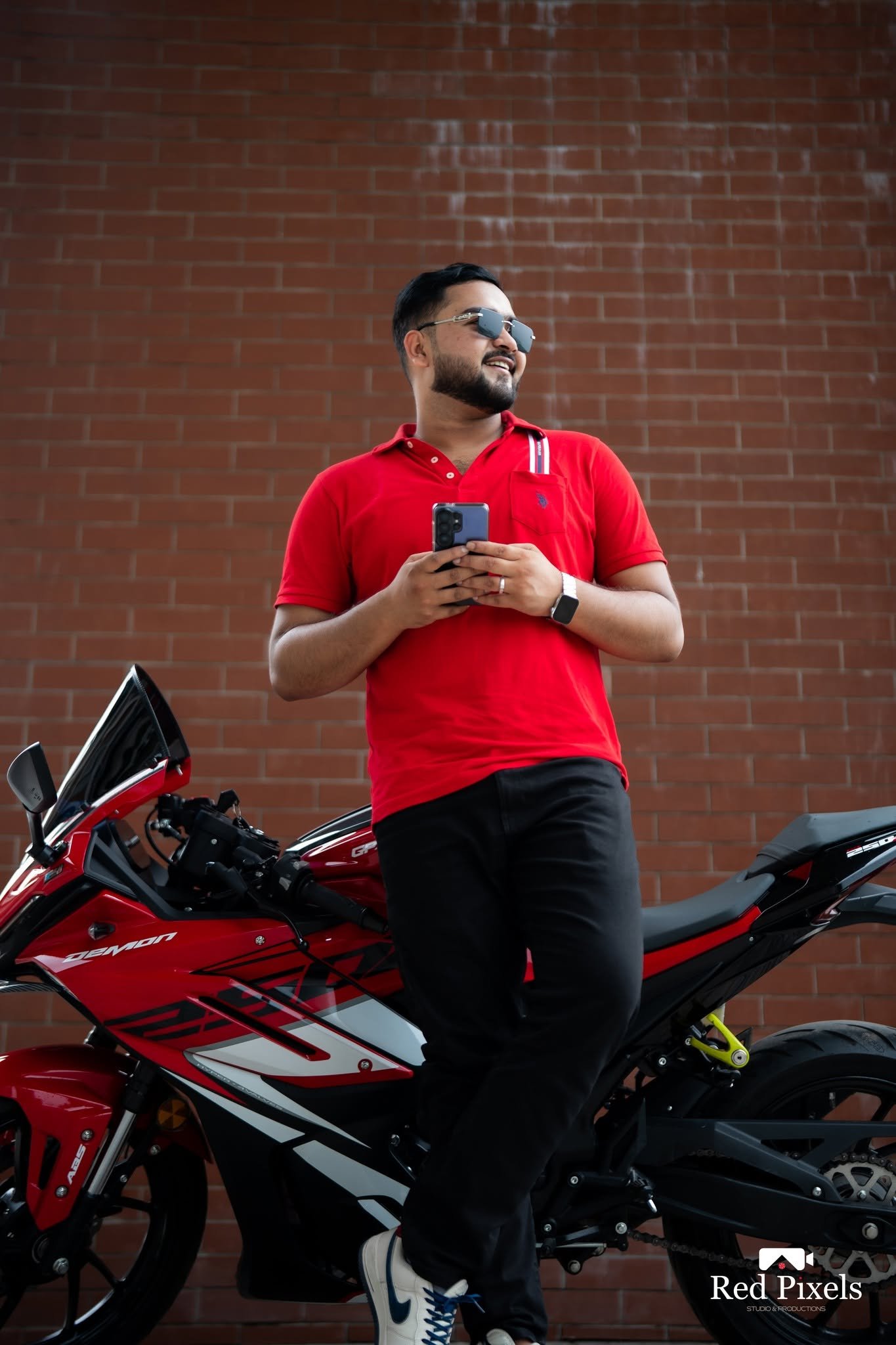 Man in a red polo leaning on a red sport motorcycle by a brick wall