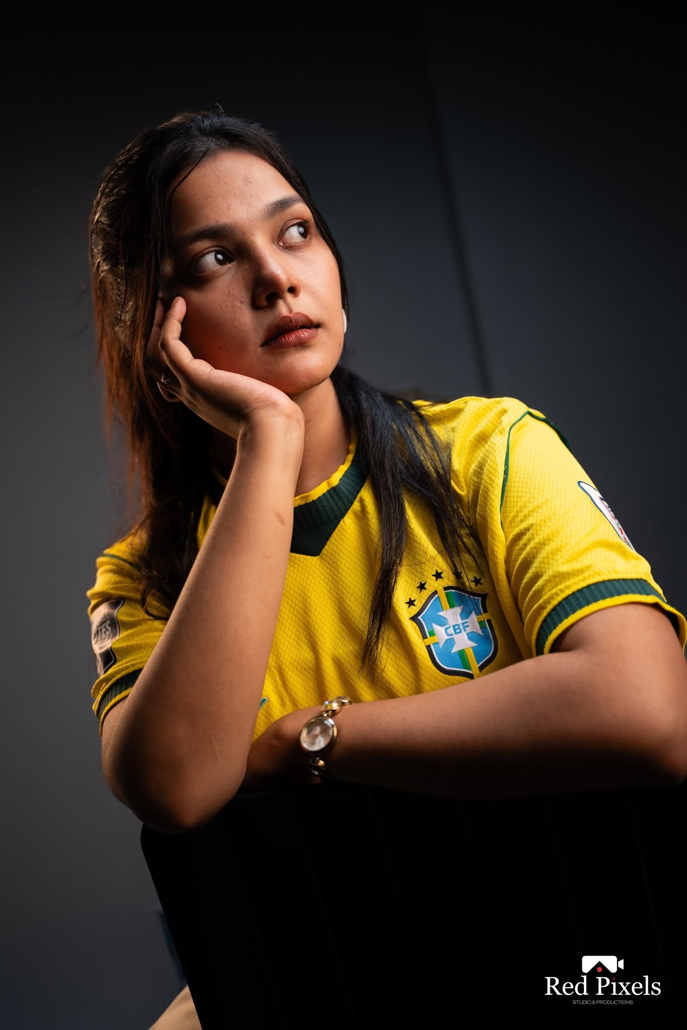 Studio portrait of a woman in a yellow jersey resting her chin on her hand